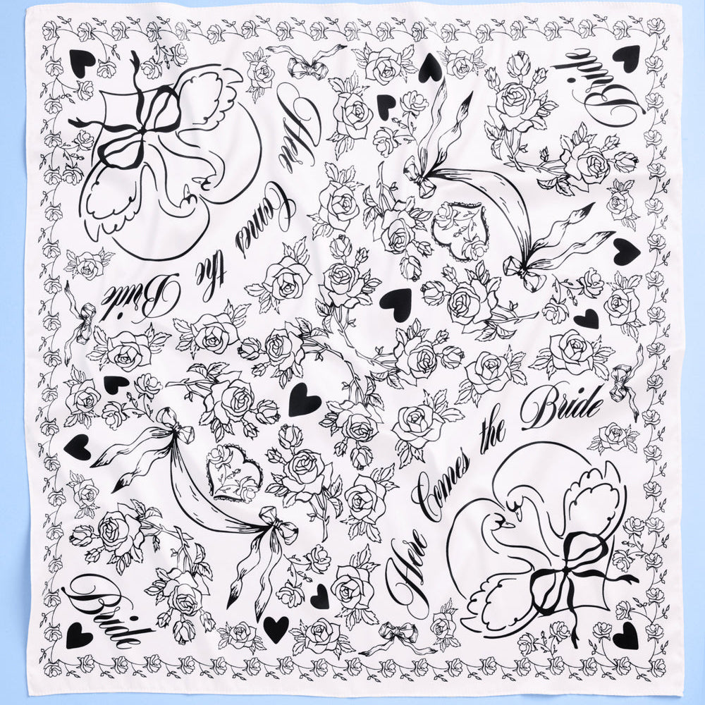 Ivory silk bridal scarf with black swan and “Bride” script design folded on blue background