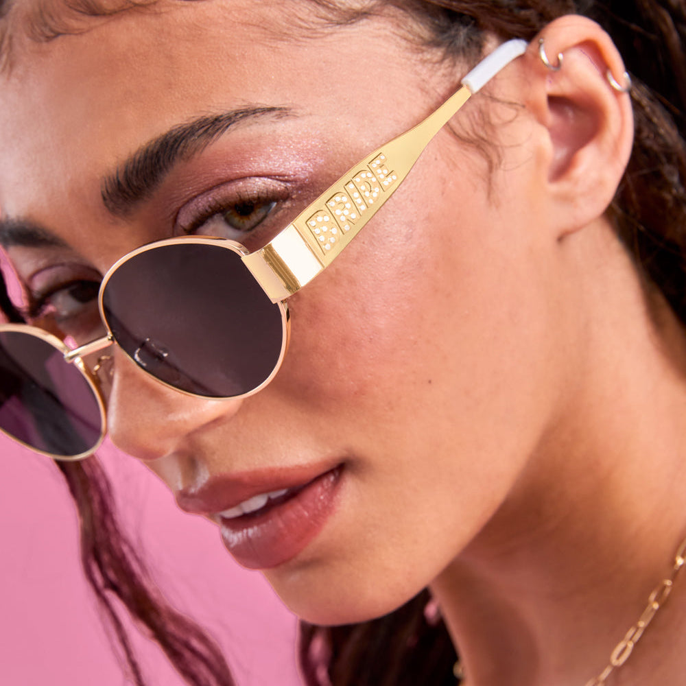 Close-up of a person wearing gold sunglasses with a pink background