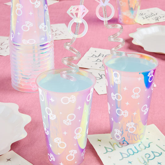 Iridescent cups with bow and ring designs on a pink tablecloth.