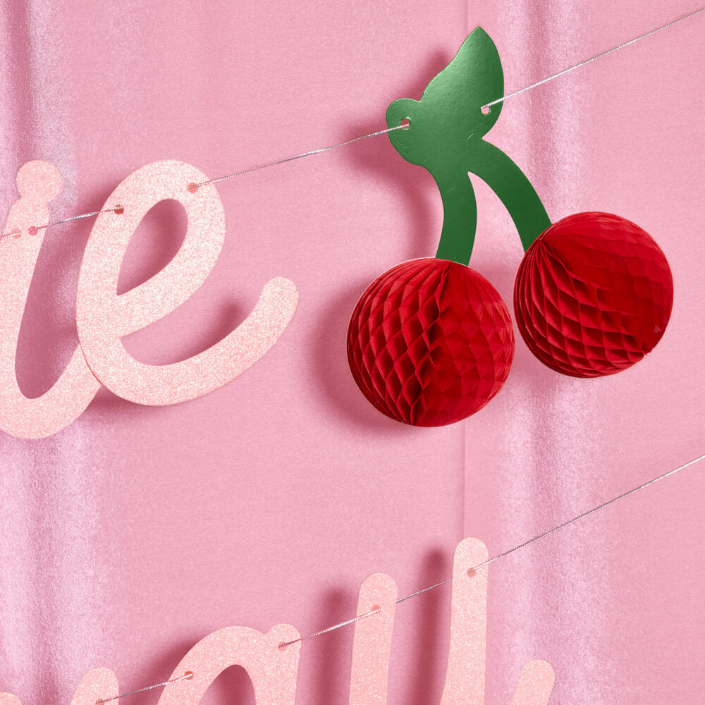 Decorative banner with red honeycomb cherries and pink letters on a pink background