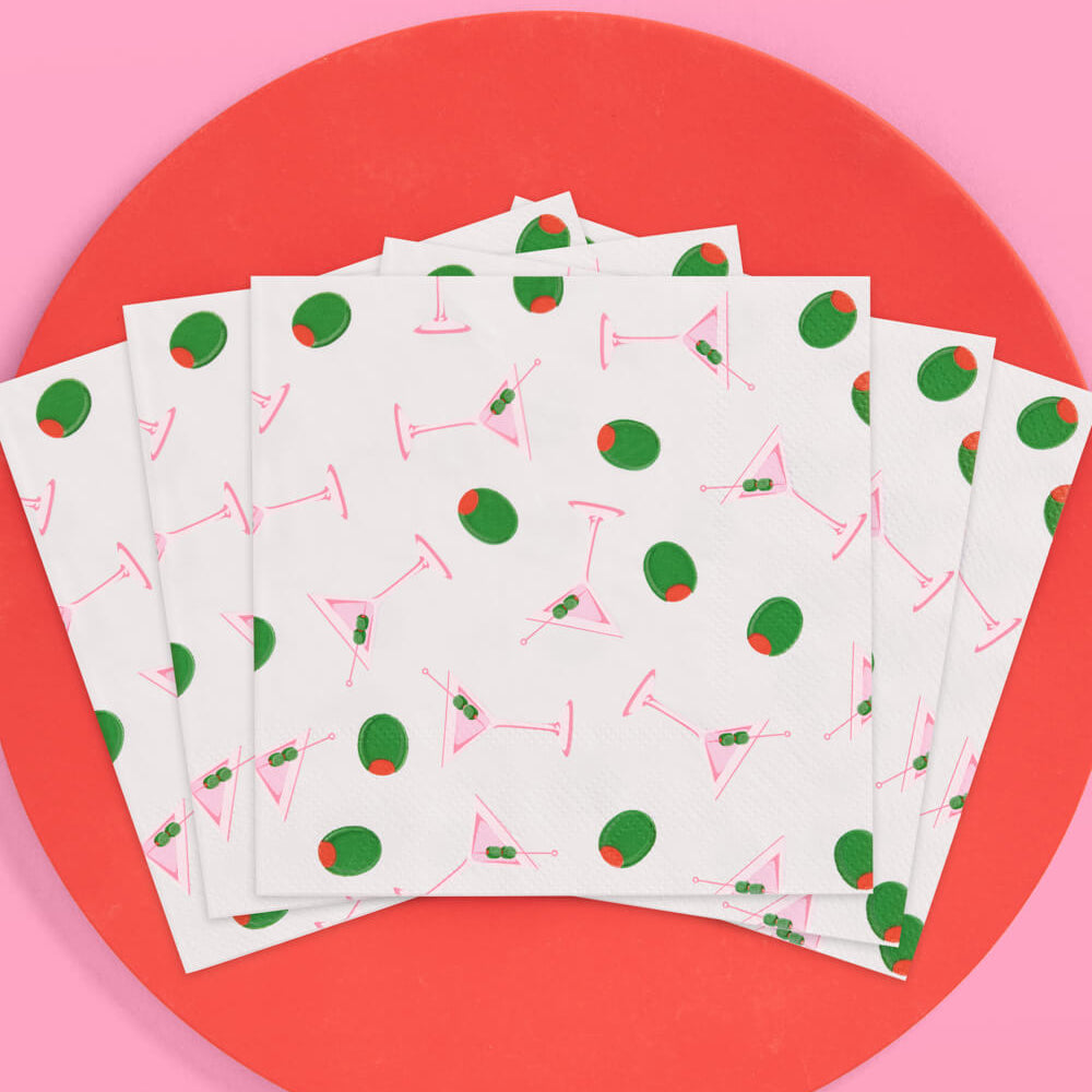 Stack of paper napkins with cocktail pattern and olives on a pink and red background