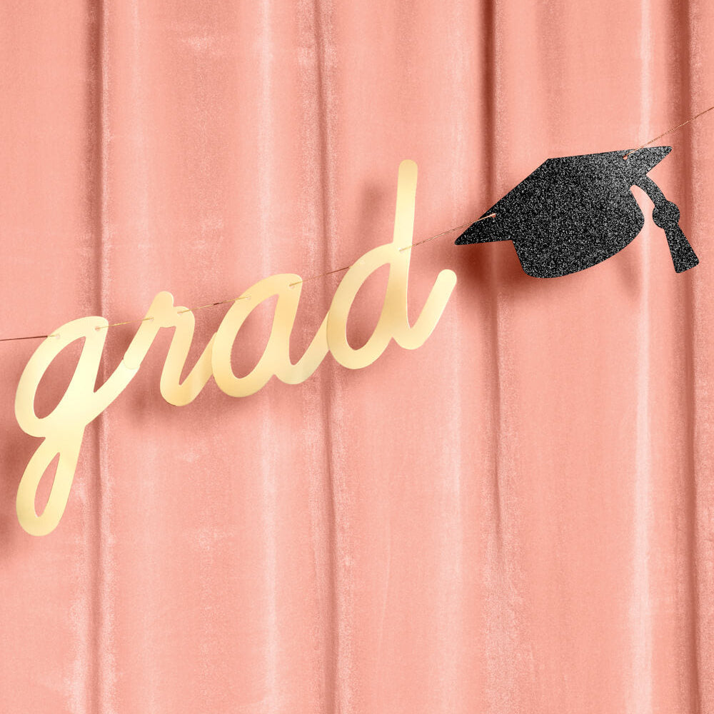 Graduation-themed decor with 'grad' in gold and a black graduation cap on a pink background
