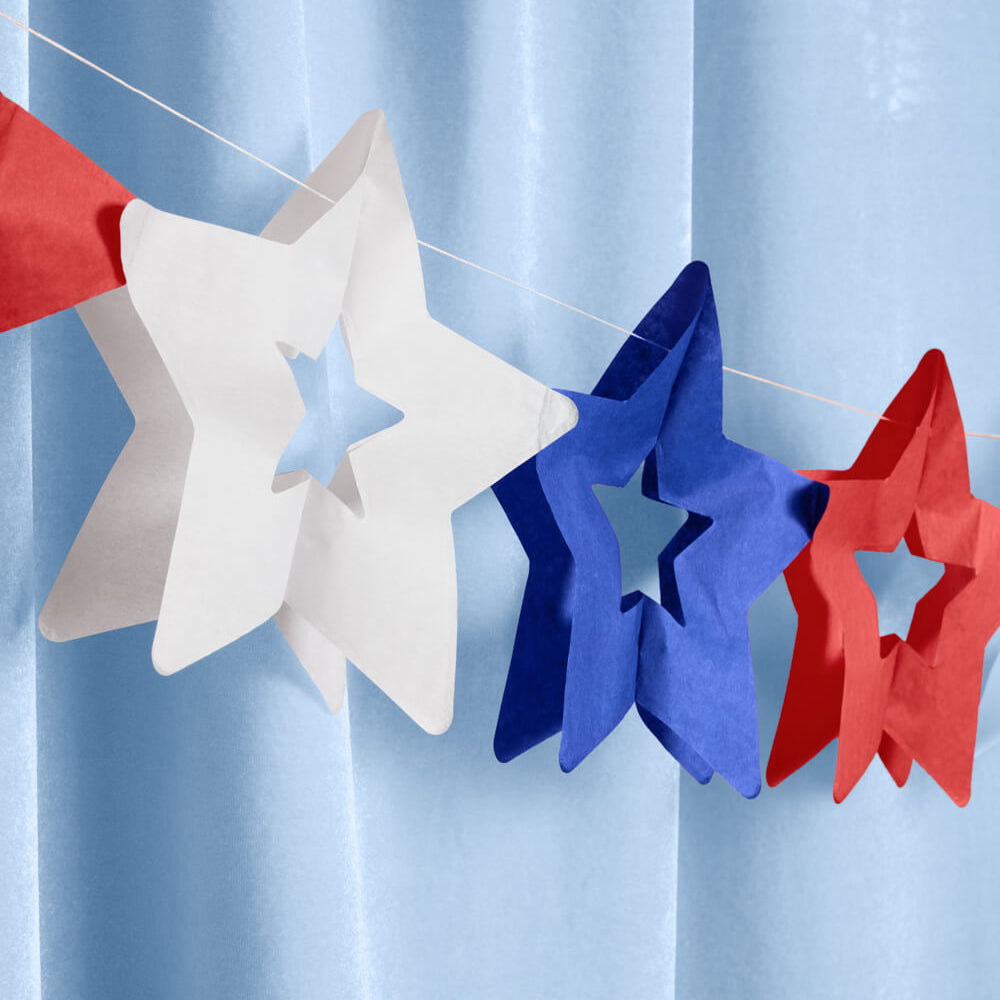 Star-shaped decorations in red, white, and blue on a string against a light blue curtain.
