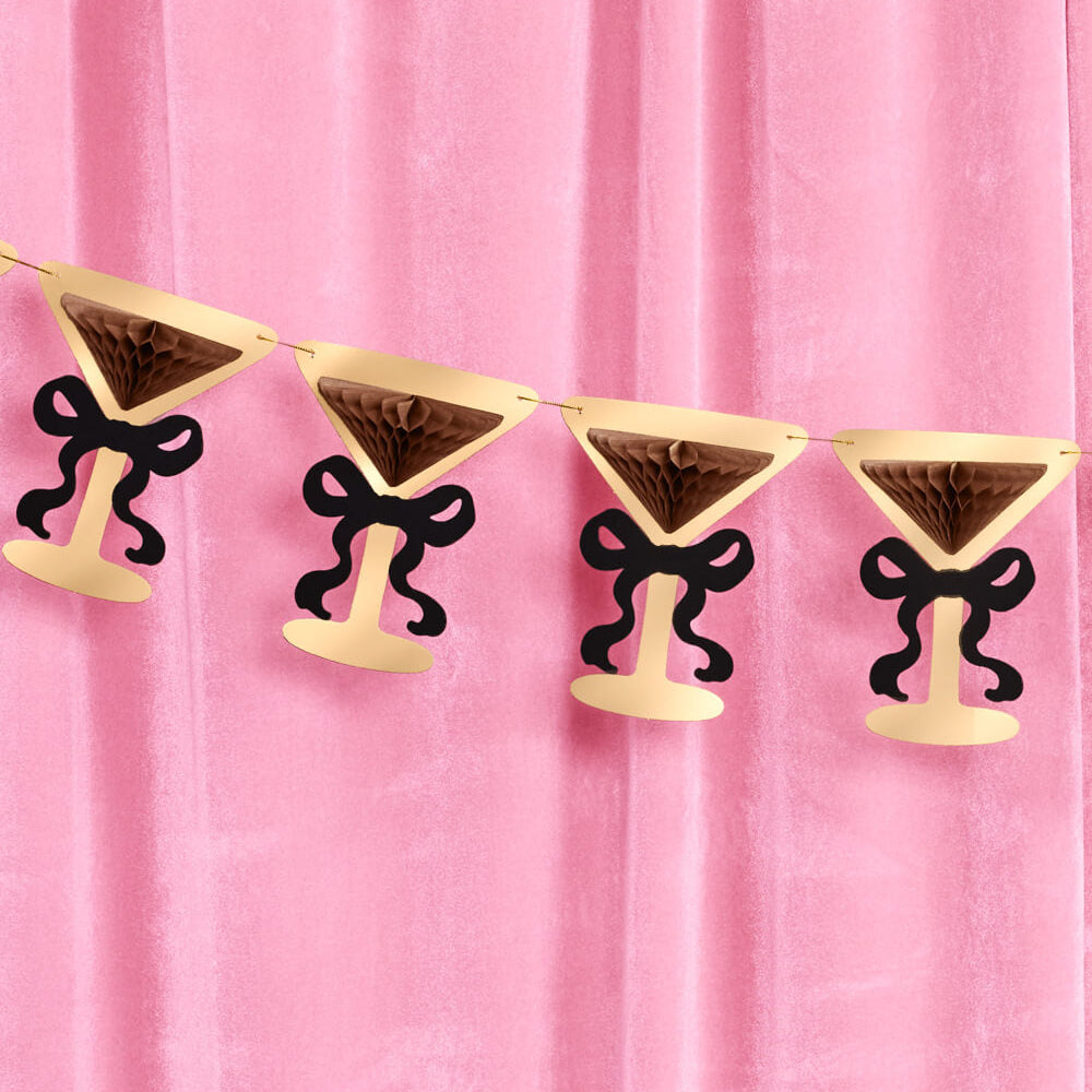 Decorative banner with martini glass shapes and black bows against a pink curtain.