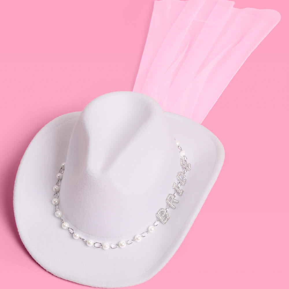 White cowboy hat with pearl necklace on a pink background