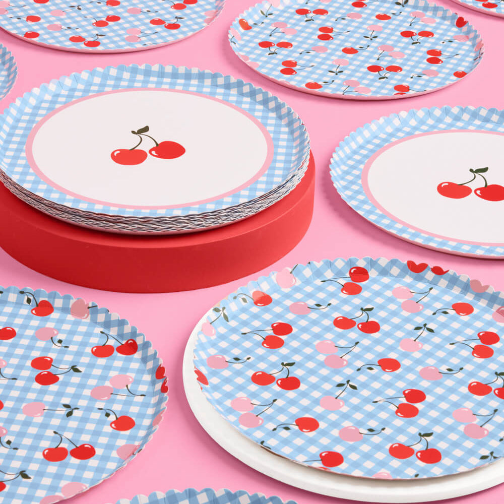 Stacks of paper plates with cherry and checkered pattern on a pink background