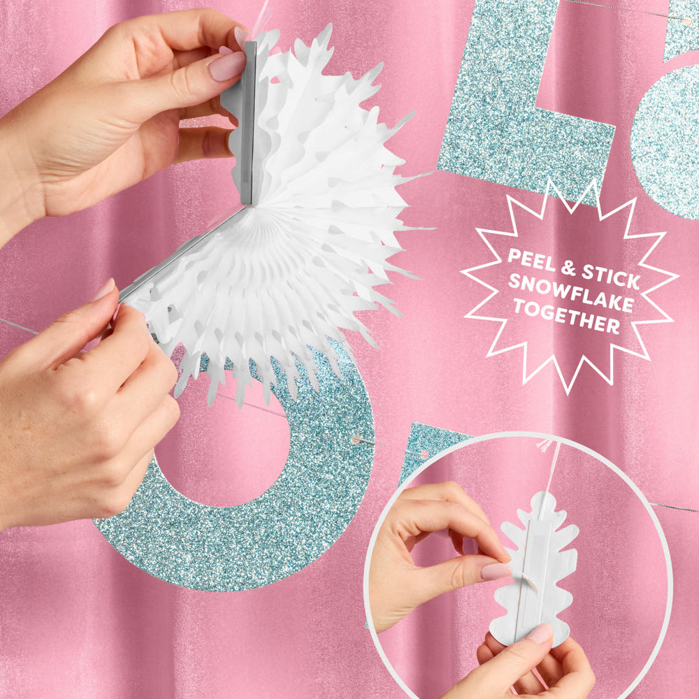 Hands attaching a snowflake decoration to a string with a pink background