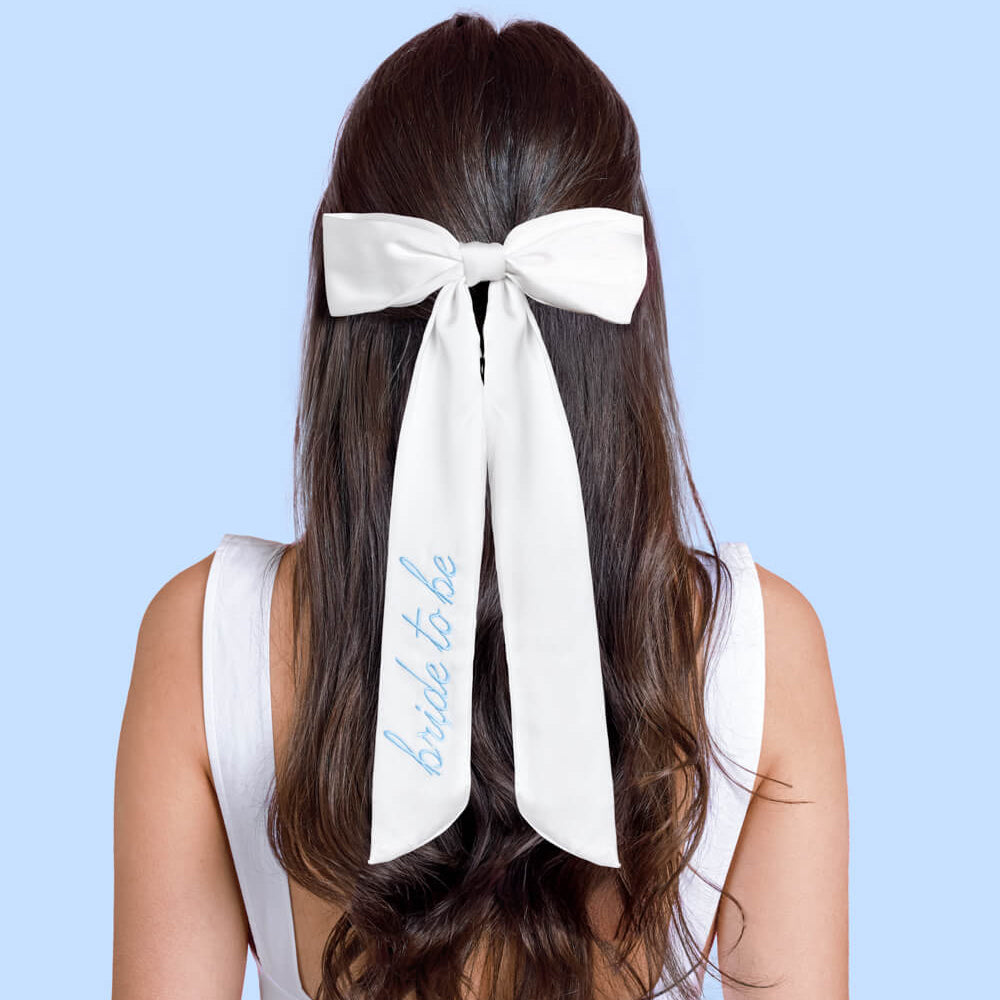 Woman with a white bow in her hair that says 'bride to be' on a light blue background
