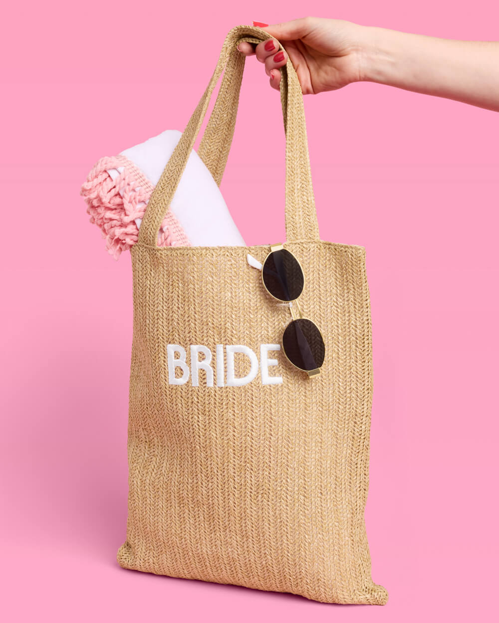 Jute bag labeled 'BRIDE' with sunglasses and a pink flower on a pink background