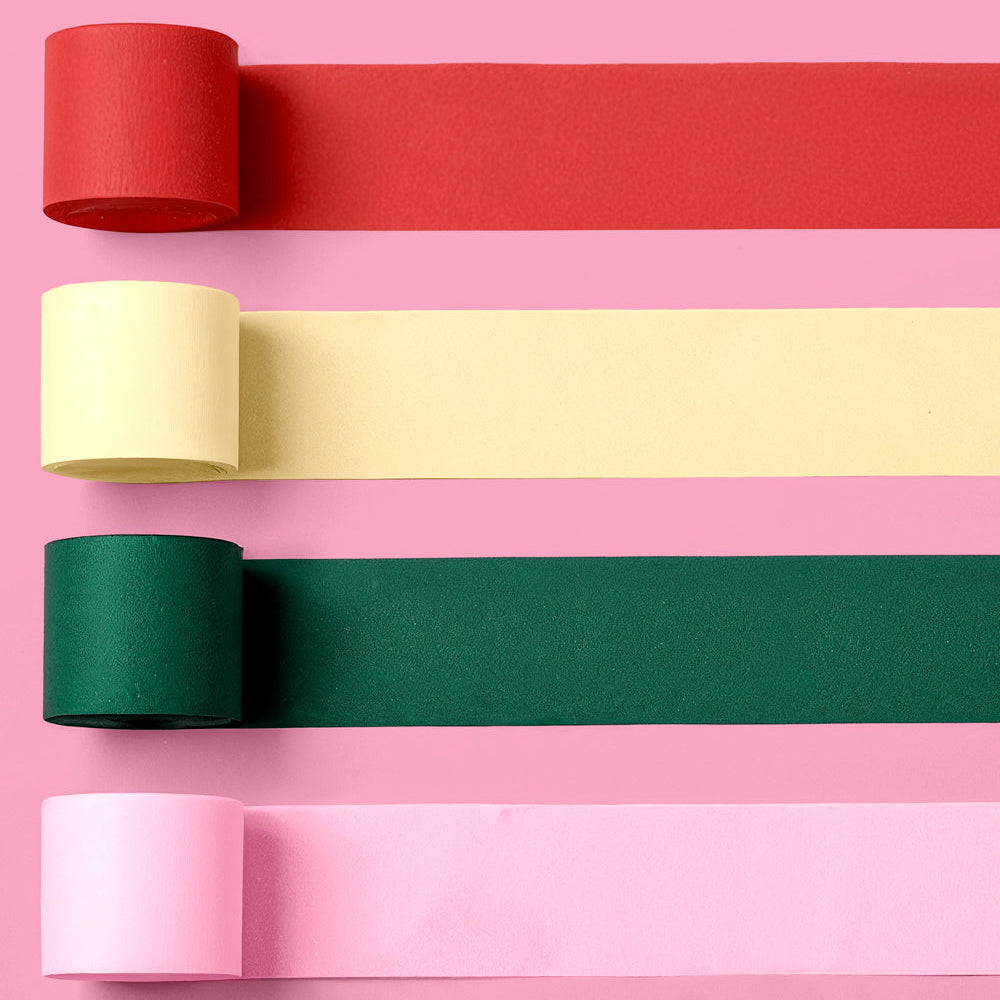 Four rolls of colored streamers in red, yellow, green, and pink on a pink background