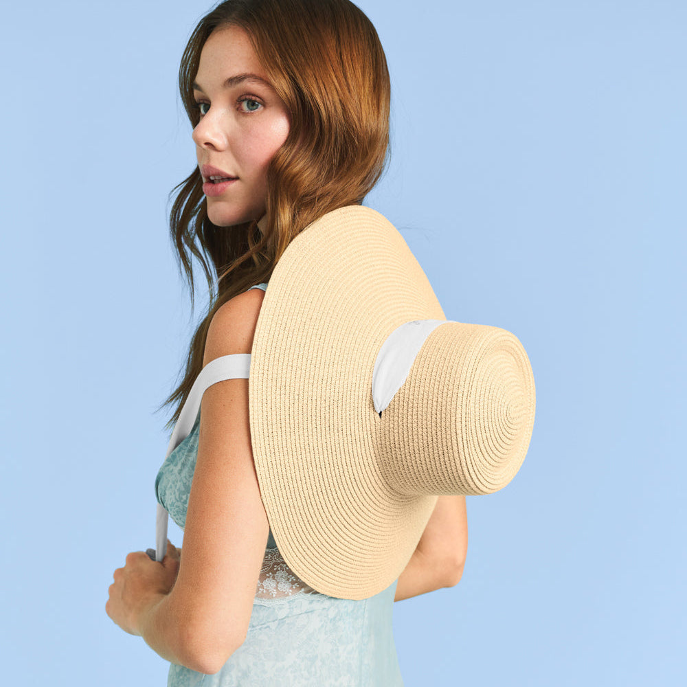 Woman holding a large straw hat against a light blue background