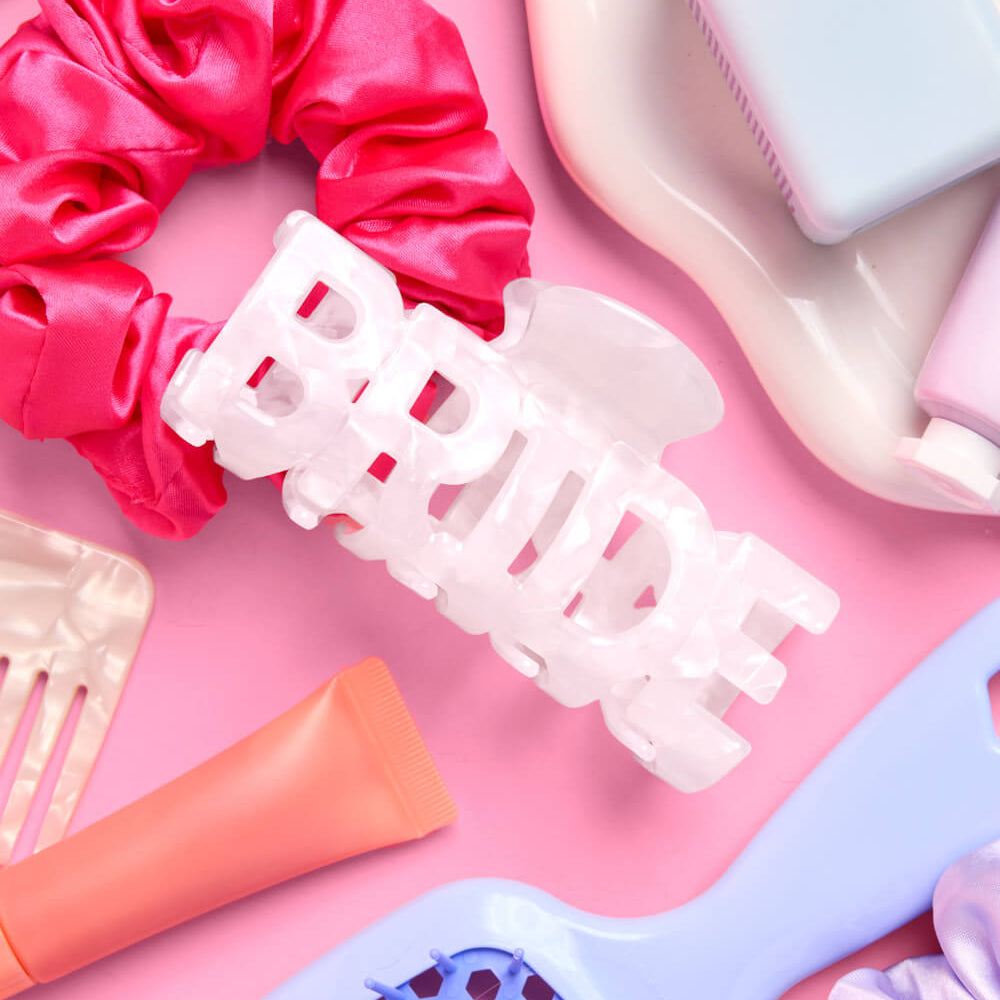 Collection of hair care products including a pink scrunchie, white clip, and orange tube on a pink background.