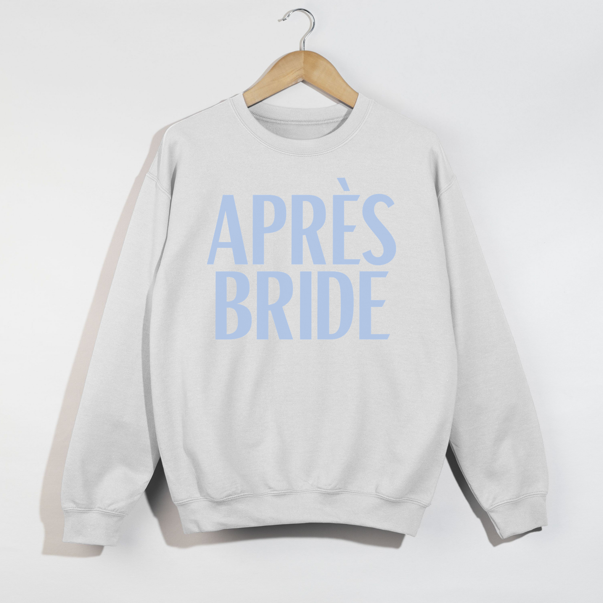 White Après Bride sweatshirt with blue lettering displayed on wooden hanger