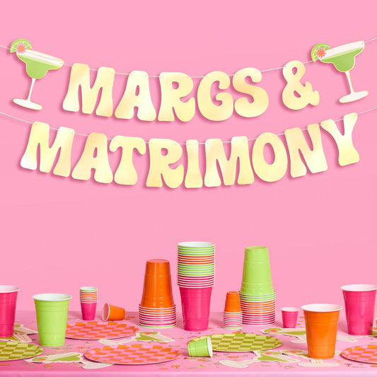 Party setup with colorful cups and 'MARGS & MATRIMONY' banner on a pink background
