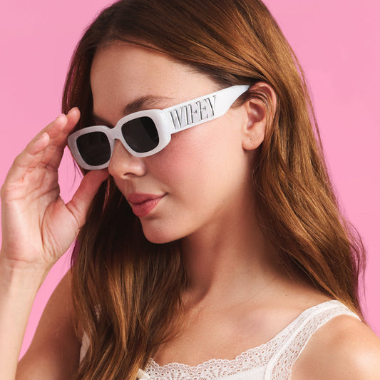 Woman wearing white sunglasses with a pink background