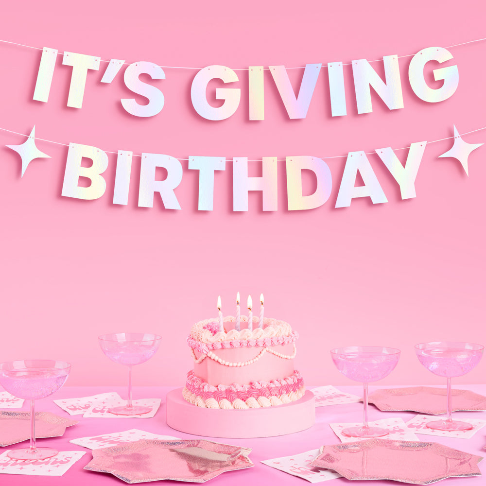 Birthday celebration with cake, pink tableware, and 'It's Giving Birthday' banner on a pink background