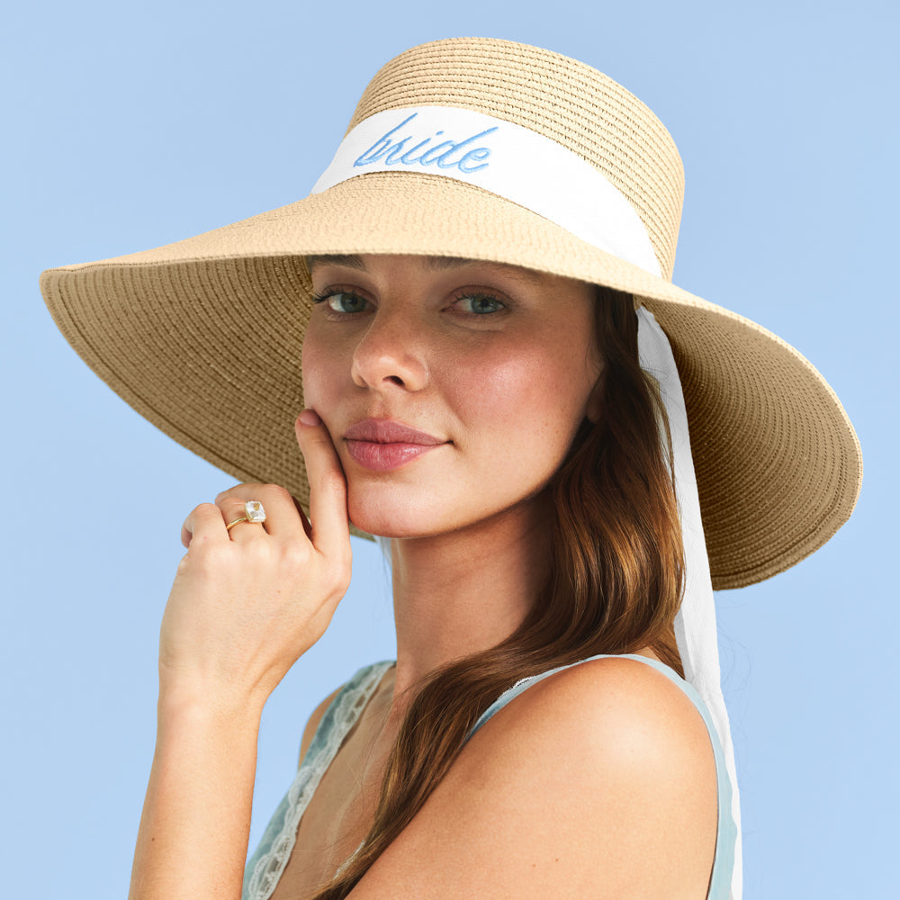 Woman wearing a straw hat with 'bride' band against a blue background