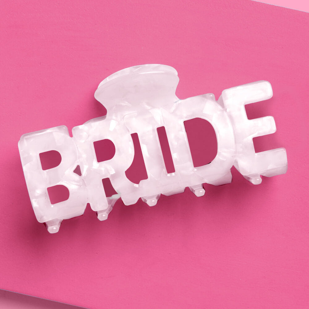 White 'BRIDE' hair clip on a pink background