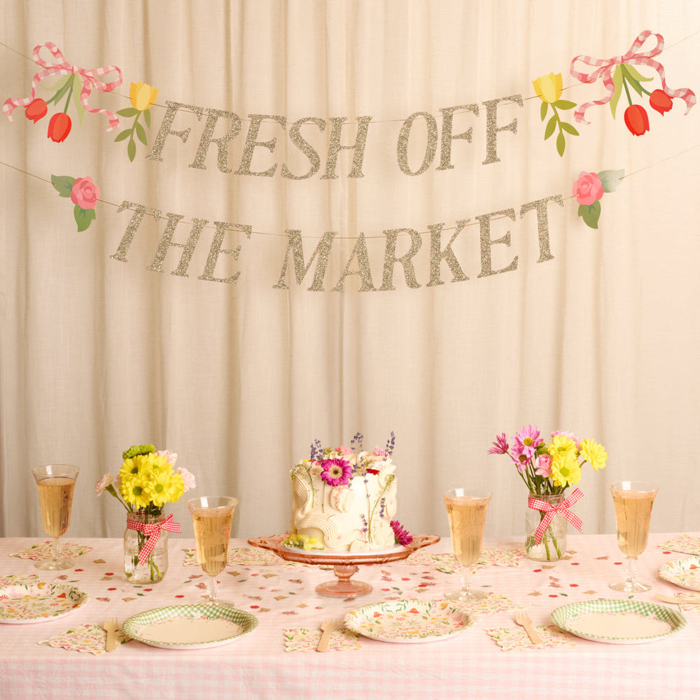 Decorated table with floral arrangements and 'Fresh Off The Market' sign against a beige curtain.
