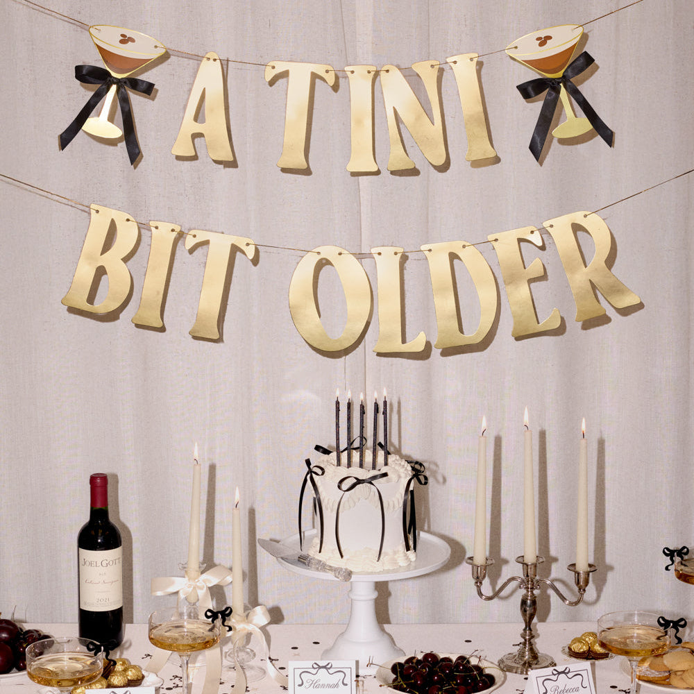 Decorated table with 'A Tini Bit Older' banner, cake, and wine bottle.