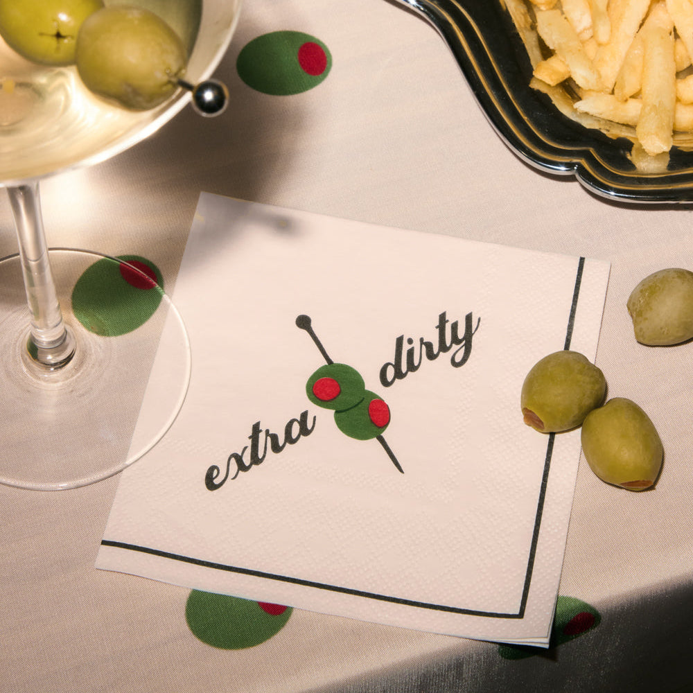 Napkin with 'extra dirty' text and olives, next to a cocktail and fries on a table.