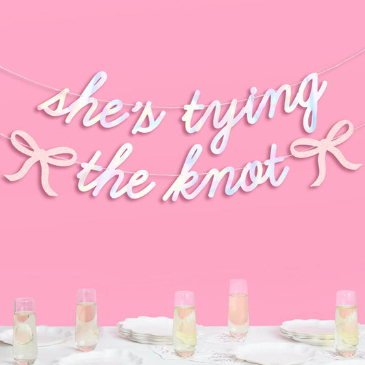 Decorative banner with 'she's tying the knot' text over a table setting with champagne glasses on a pink background.