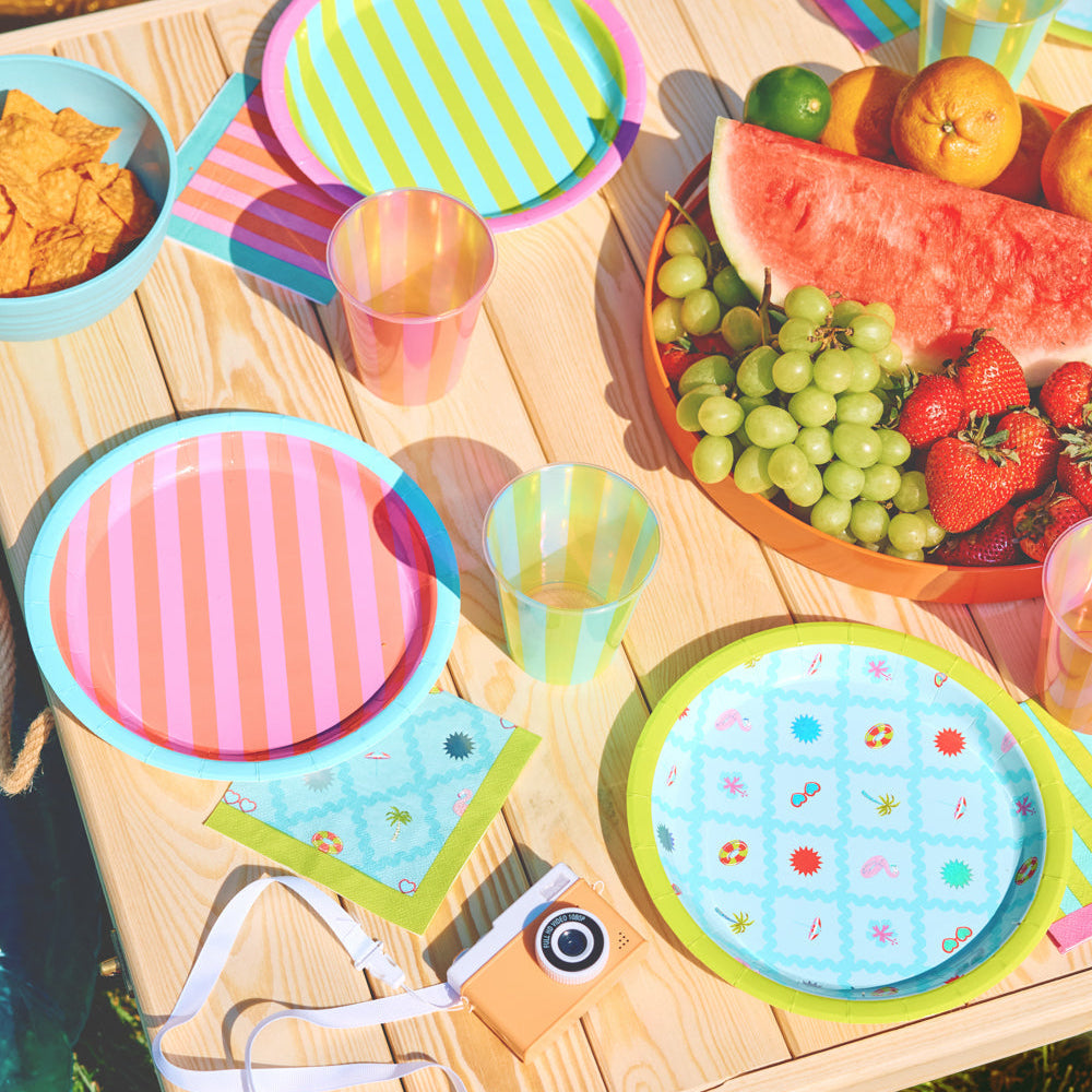 Colorful children's plates, cups, and napkins on a wooden table with fruits.