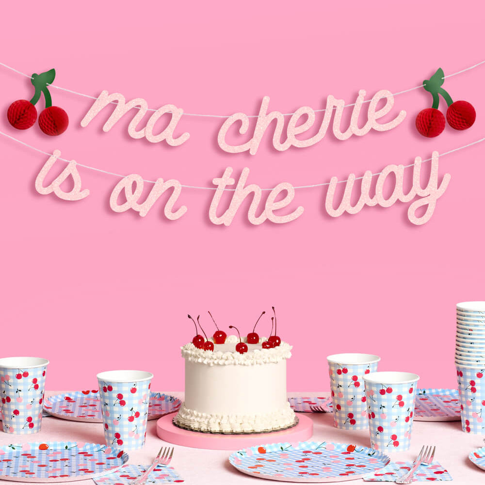 Pink background with 'ma chérie is on the way' banner, cake, and partyware.