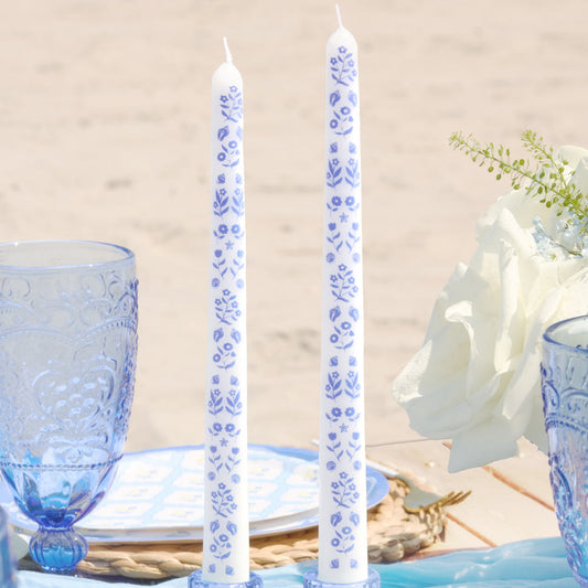 Decorative candles with blue floral patterns on a table setting with blue glasses and plates.