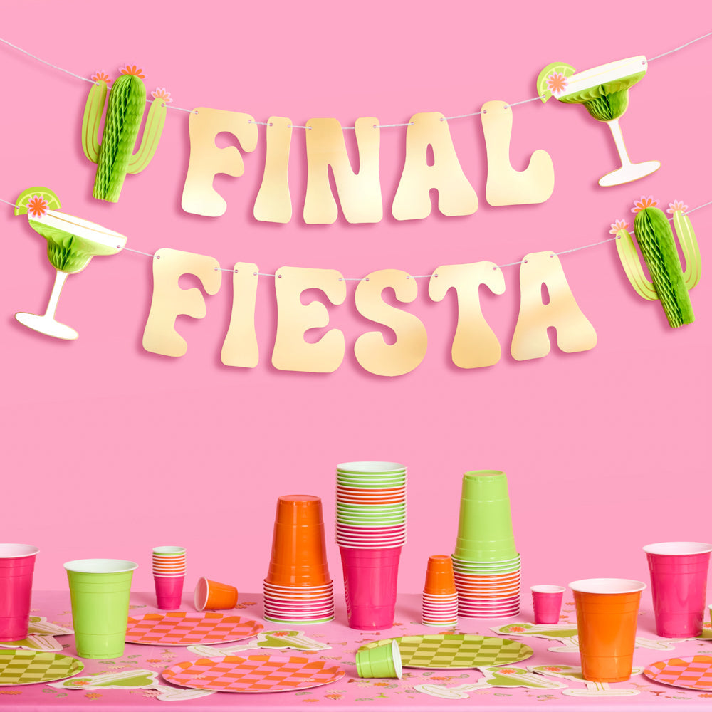 Party setup with 'Final Fiesta' banner, cups, and decorations on a pink background