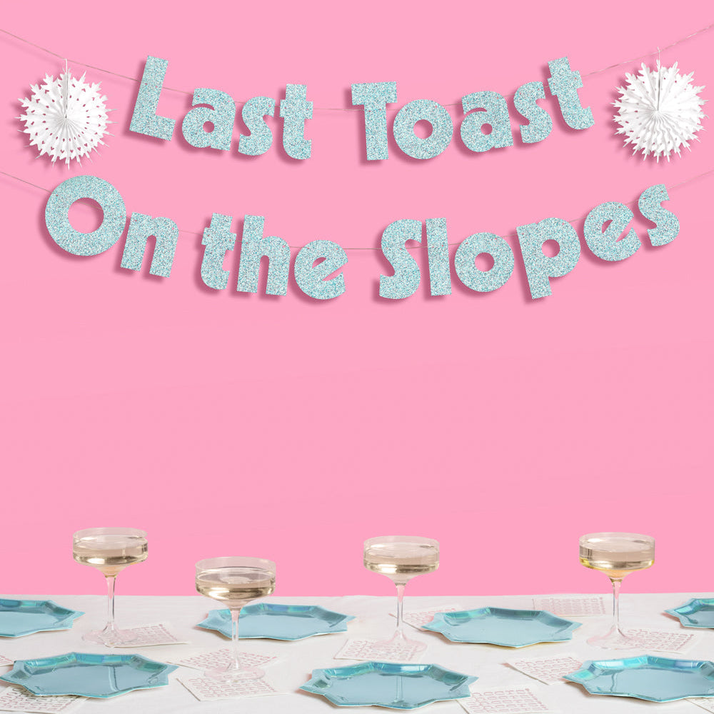 Decorative banner with 'Last Toast On the Slopes' text above a table setting with glasses and plates on a pink background.