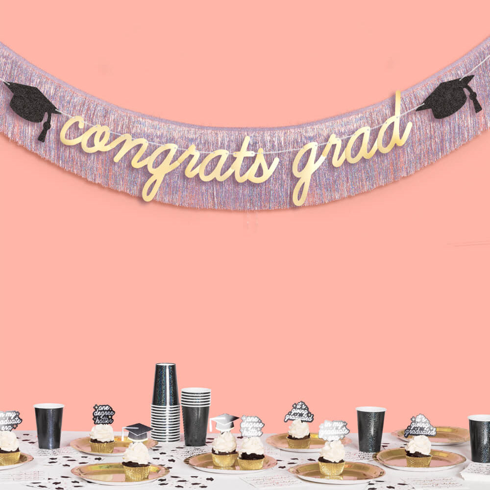 Graduation-themed banner with 'congrats grad' on a pink background, above a table with graduation-themed decorations.