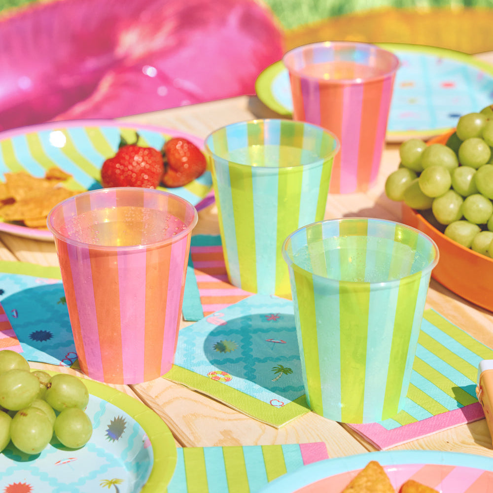 Colorful plastic cups and plates on a picnic table with snacks and fruits.