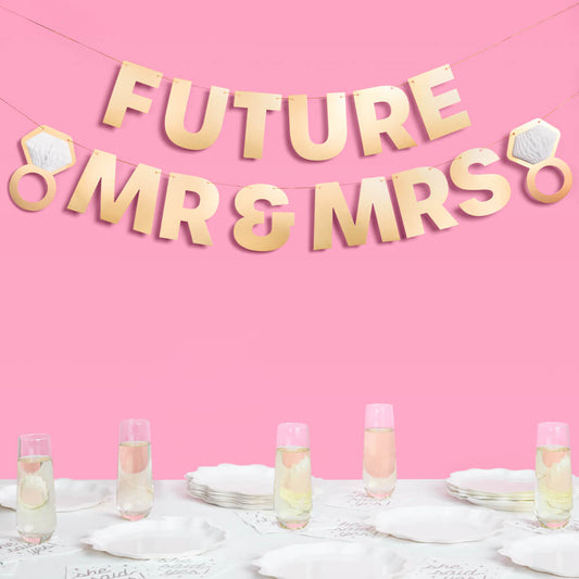 Decorative banner with 'Future Mr & Mrs' on a pink background, with glasses of champagne on a table.