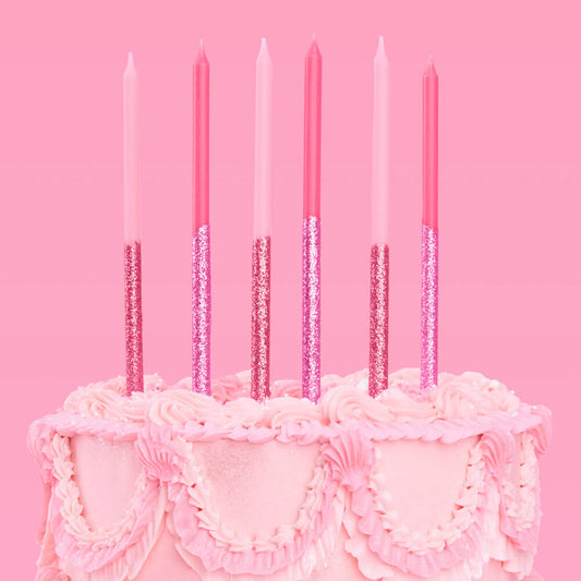 Pink birthday cake with lit candles against a pink background