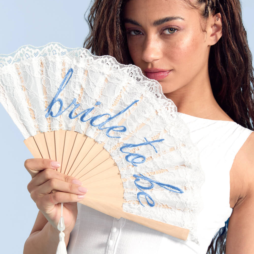 Woman holding a lace fan with 'bride to be' text against a light blue background