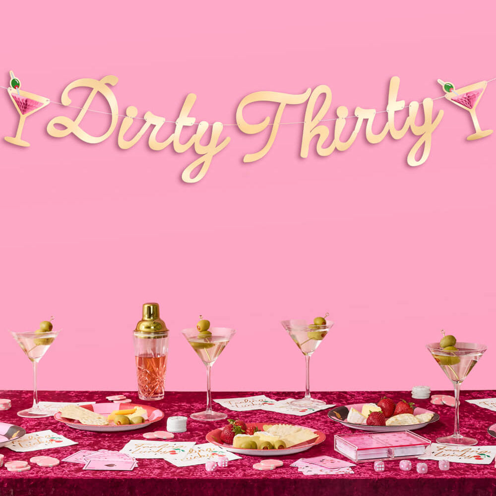 Decorative 'Dirty Thirty' sign with a table set for a celebration on a pink background.
