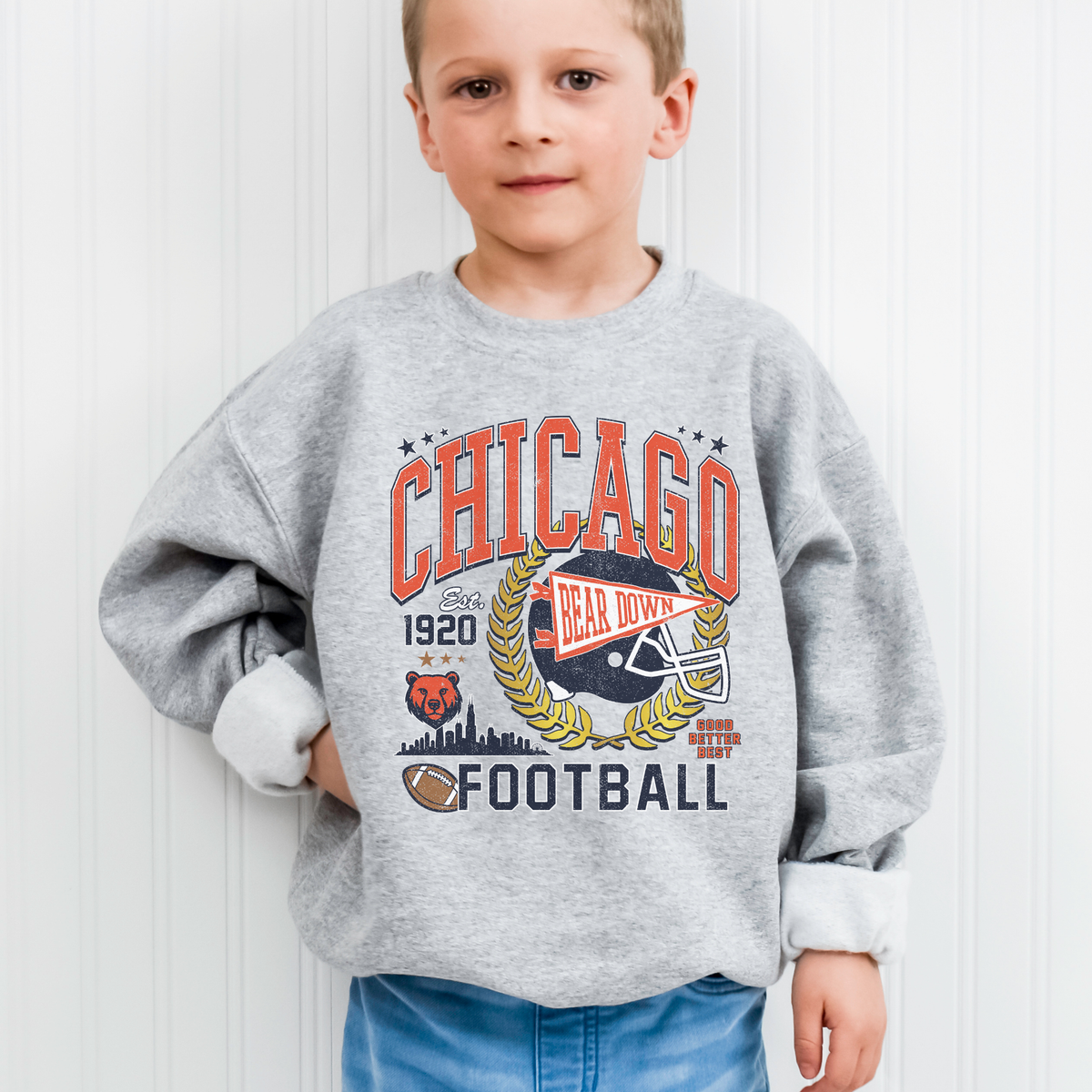 Child wearing a gray sweatshirt with 'Chicago Football' design against a white wall.