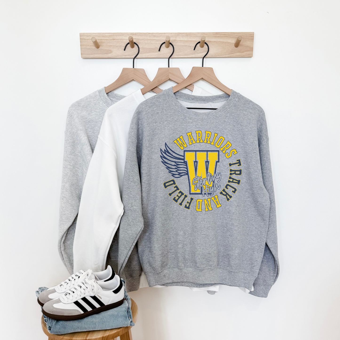 Gray sweatshirt with 'Warriors Track & Field' design, white shirt, and Adidas sneakers on a white background.