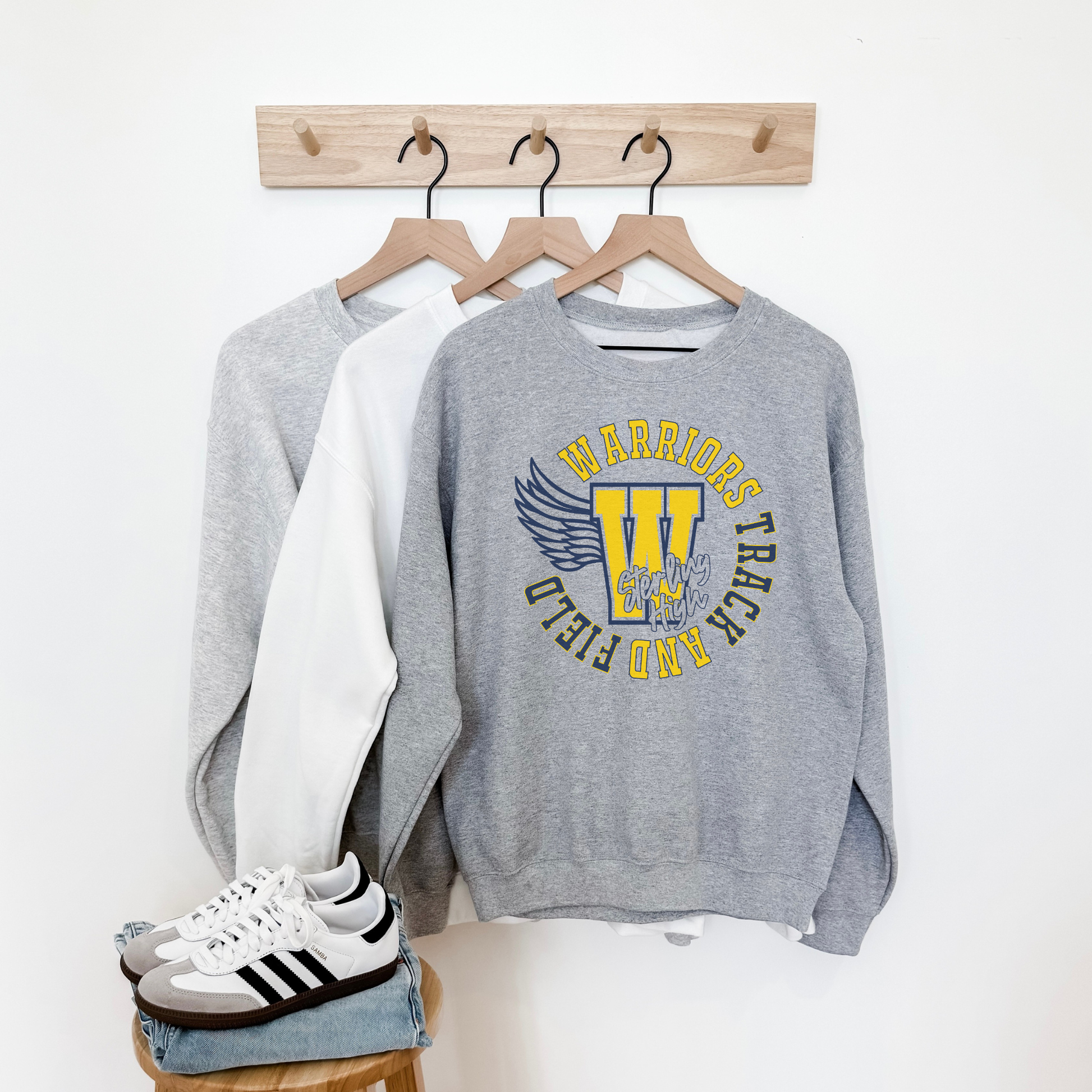 Gray sweatshirt with 'Warriors Track & Field' design, white shirt, and Adidas sneakers on a white background.