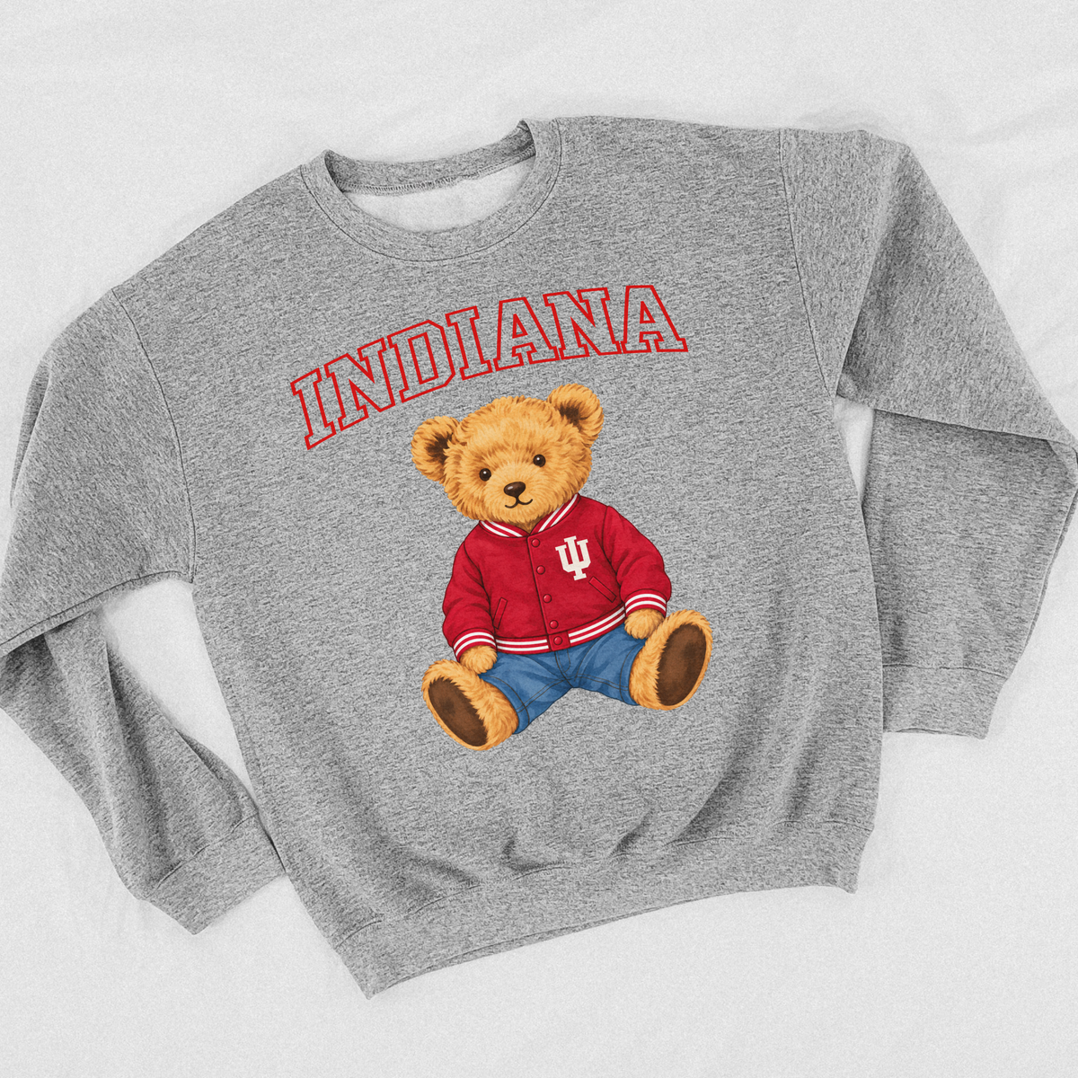 Sport grey Indiana Hoosiers teddy bear crewneck sweatshirt laid flat, featuring a golden teddy bear in a crimson IU varsity jacket with blue jeans and arched Indiana lettering.