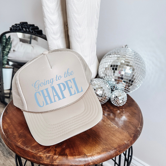 Going to the Chapel foam front trucker hat in tan with light blue bridal text displayed on wooden stool with disco balls