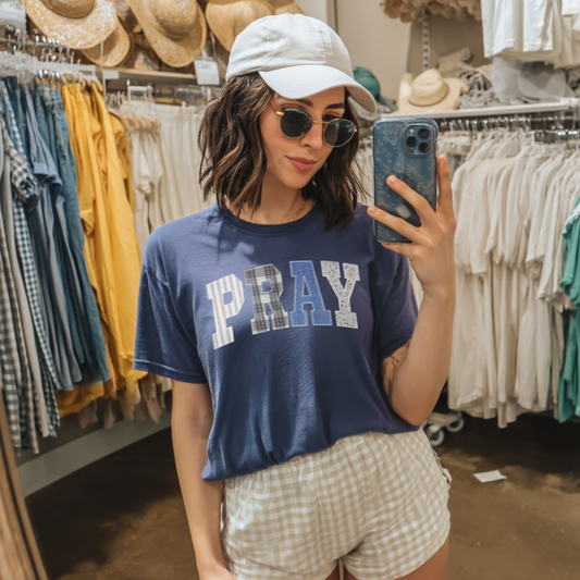 Woman wearing navy PRAY faux patchwork faith tee styled with neutral shorts