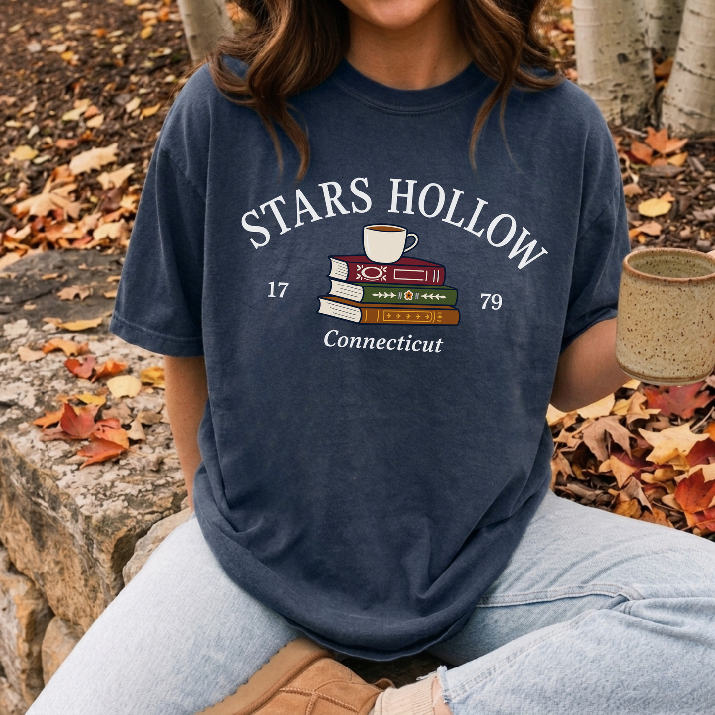 Woman wearing a True Navy Stars Hollow Connecticut graphic tee while enjoying coffee outdoors during autumn.