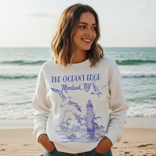 "Smiling woman at the beach wearing white Montauk ‘The Ocean’s Edge’ coastal graphic sweatshirt."