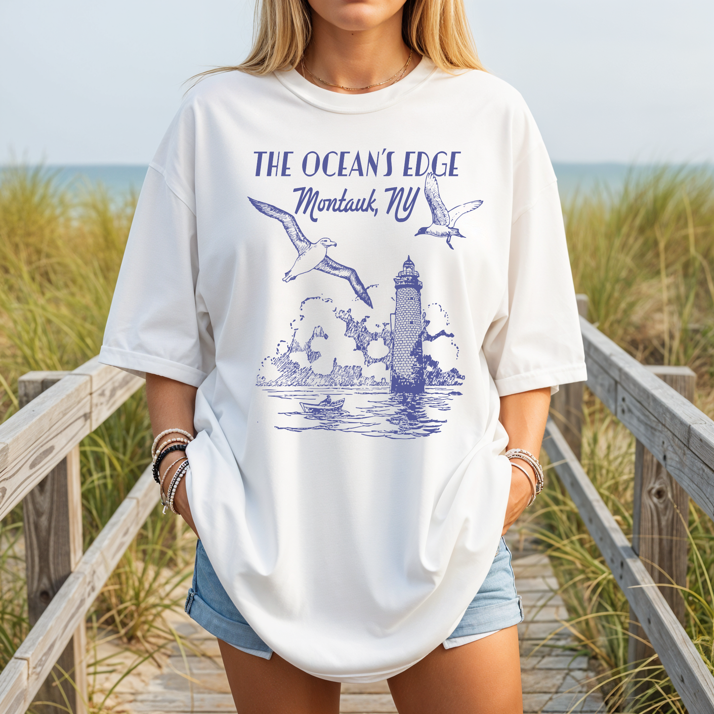 Model wearing true-to-size white Comfort Colors Montauk NY graphic tee with coastal lighthouse design at the beach.