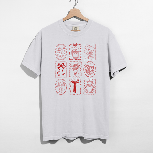 White Comfort Colors tee with red Valentine stamp icons graphic on hanger.