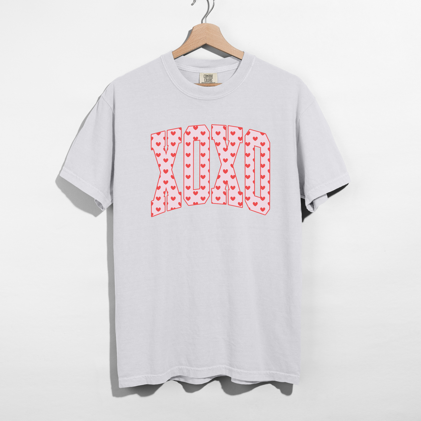 White Comfort Colors XO heart graphic t-shirt on wooden hanger