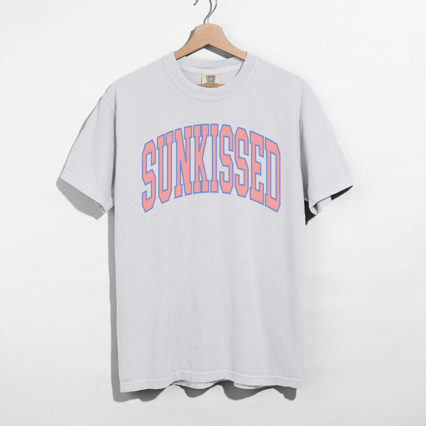 White SUNKISSED graphic t-shirt on hanger featuring pastel collegiate lettering, unisex relaxed fit tee