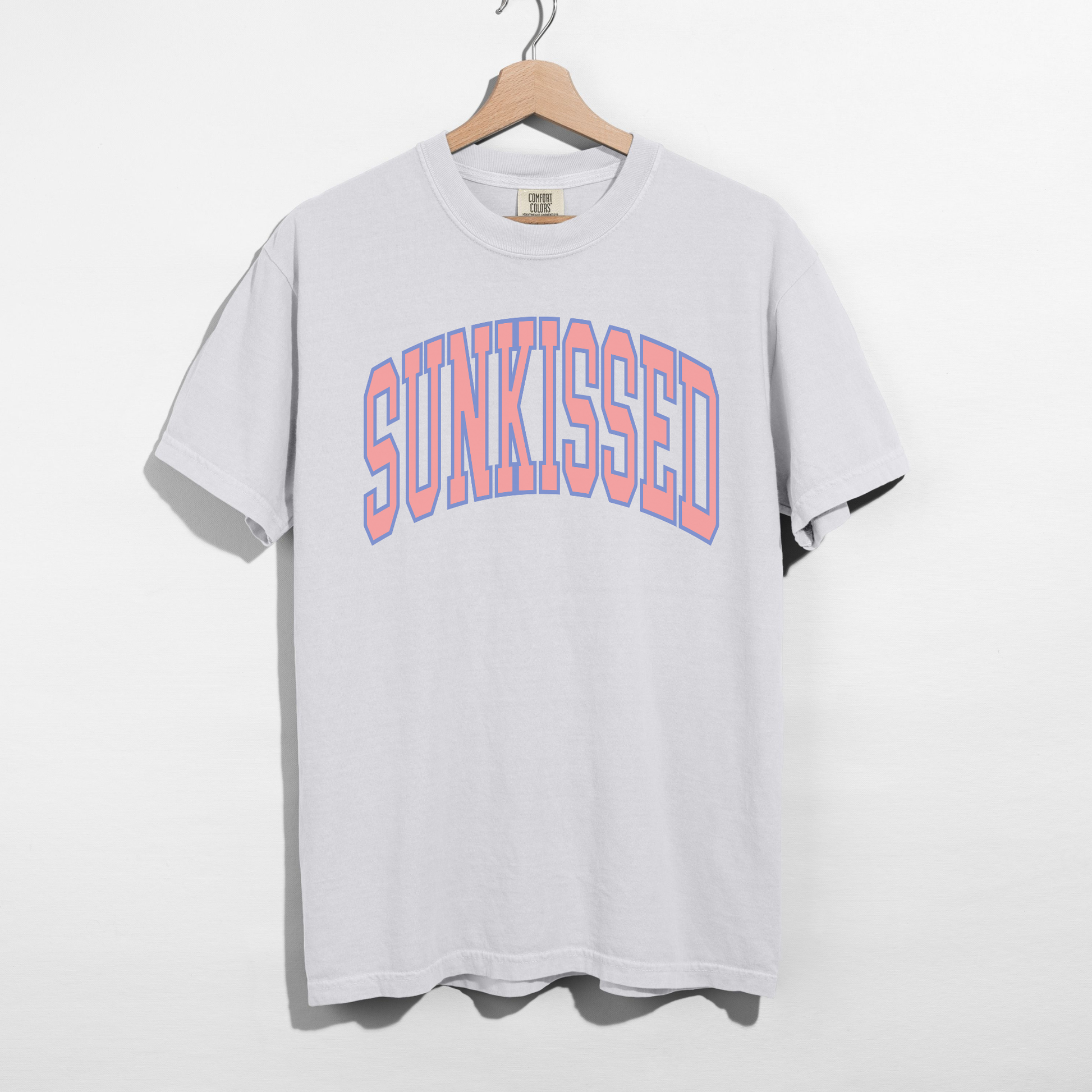 White SUNKISSED graphic t-shirt on hanger featuring pastel collegiate lettering, unisex relaxed fit tee